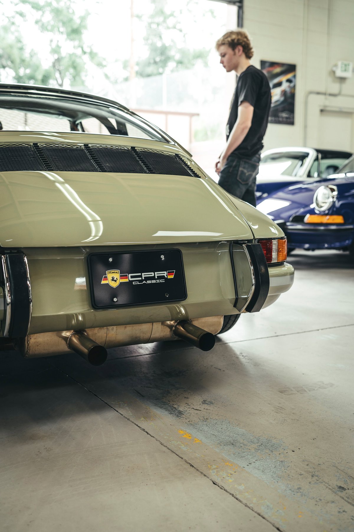 Sage green early Porsche 911 Targa rear, showing engine lid grilles, bumperettes, heat-wrapped dual exhaust, and CPR Classic plate.