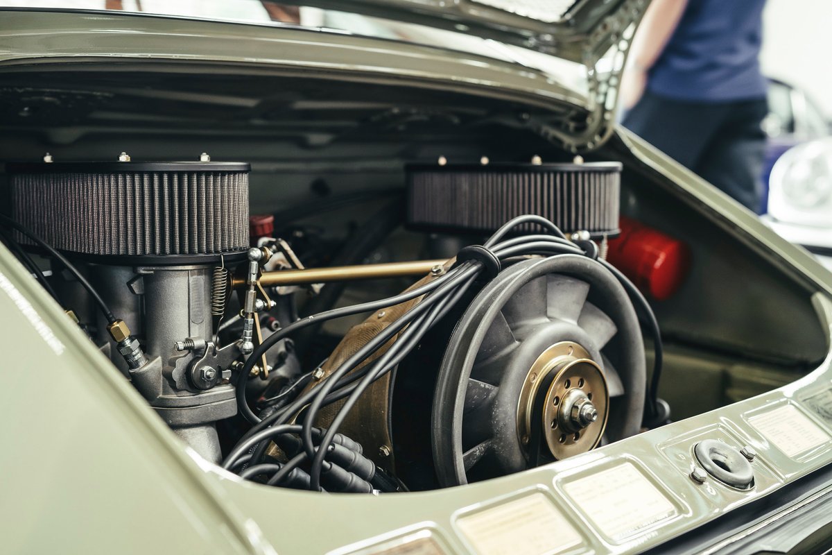 Muted green classic Porsche 911 air-cooled flat-six engine, showing dual air filters, carburetors, and cooling fan.