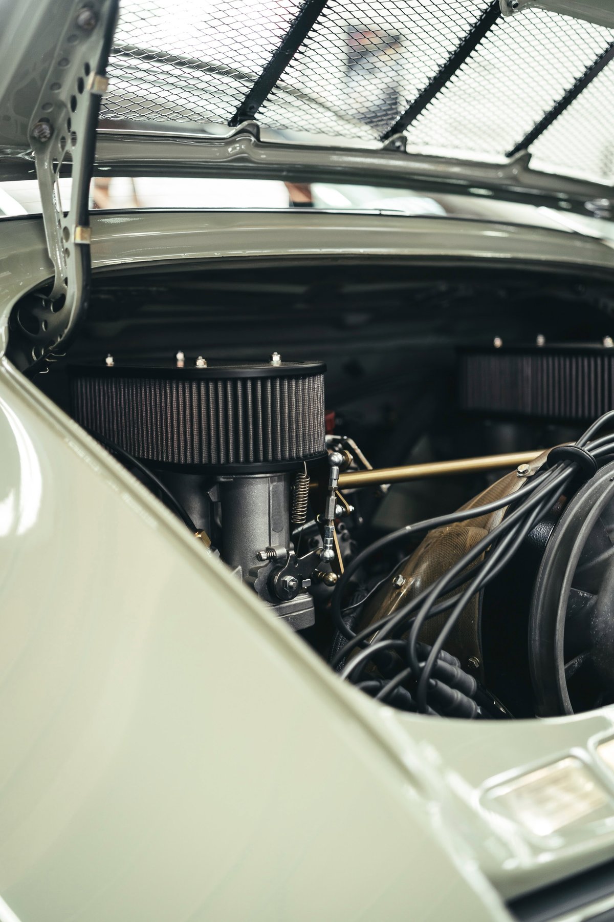 Close-up: Light green vintage Porsche 911's air-cooled flat-six engine. Dual filters, carbs & ignition wires visible under mesh grille.