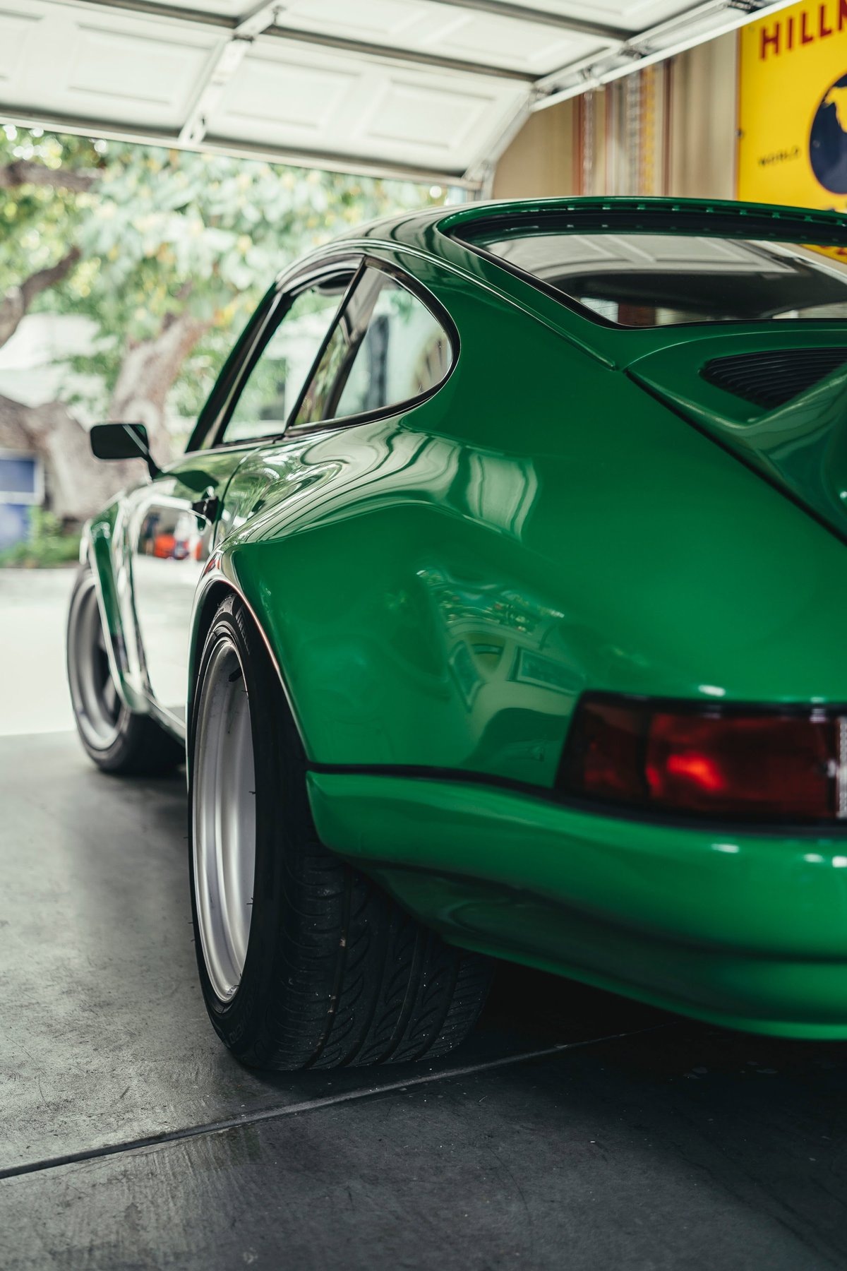 Rear-quarter view of an emerald green widebody Porsche 911 with custom deep-dish silver rims and wide tires.