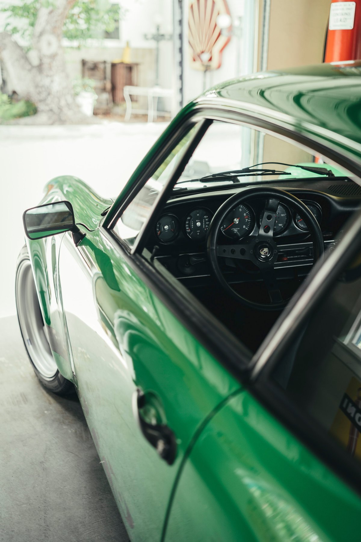 Bright green classic Porsche 911 (G-series) widebody, showcasing deep-dish custom rims and an iconic 3-spoke steering wheel.