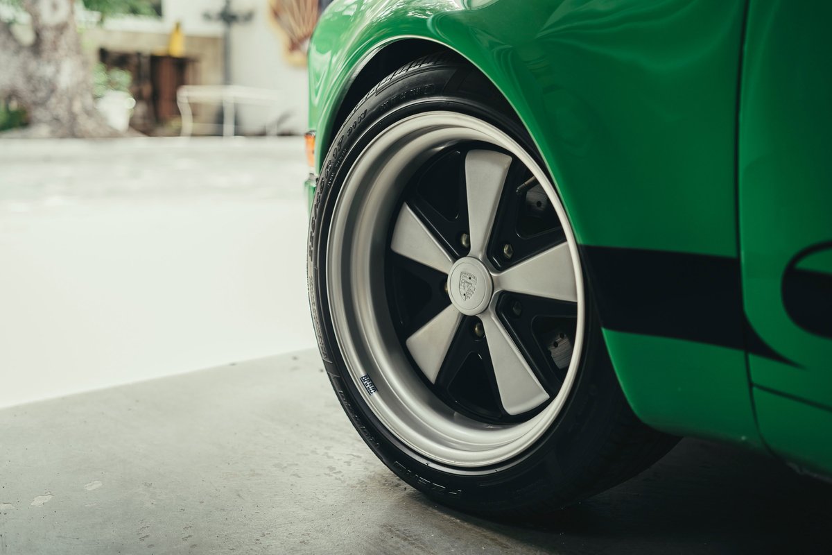Close-up of a green Porsche 911's Fuchs-style alloy rims and tire, featuring a black side livery on the fender.