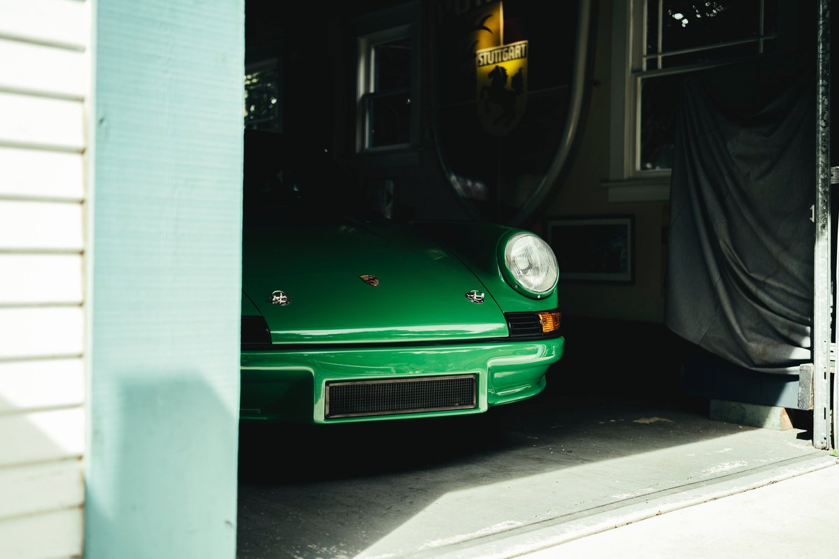Vibrant Viper Green classic Porsche 911 emerges from a garage. Its iconic round headlight, detailed front bumper, and grille are visible.