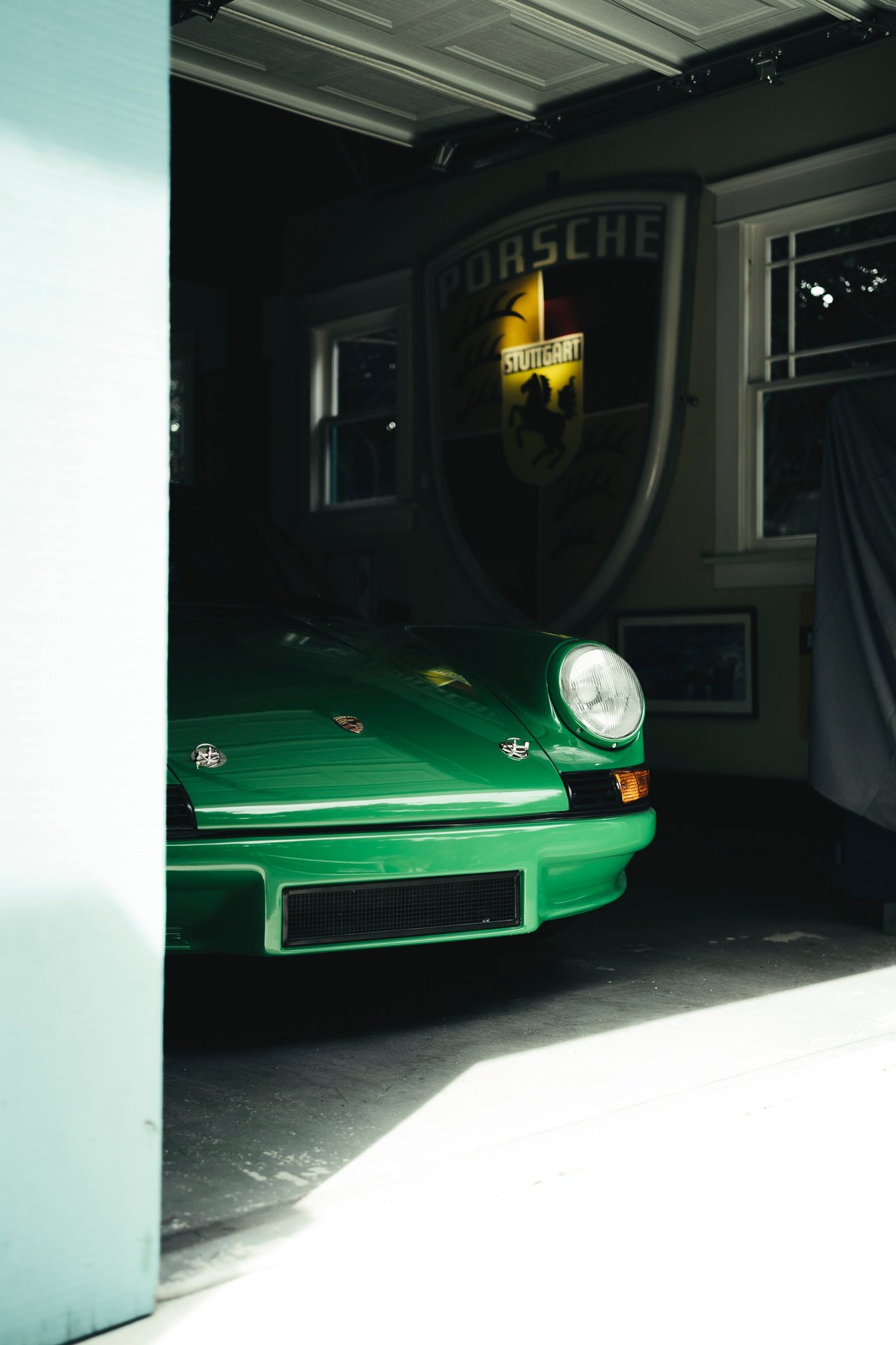 Vivid green vintage Porsche 911 peeks from garage, showcasing its signature round headlight, streamlined front bumper, and grille.