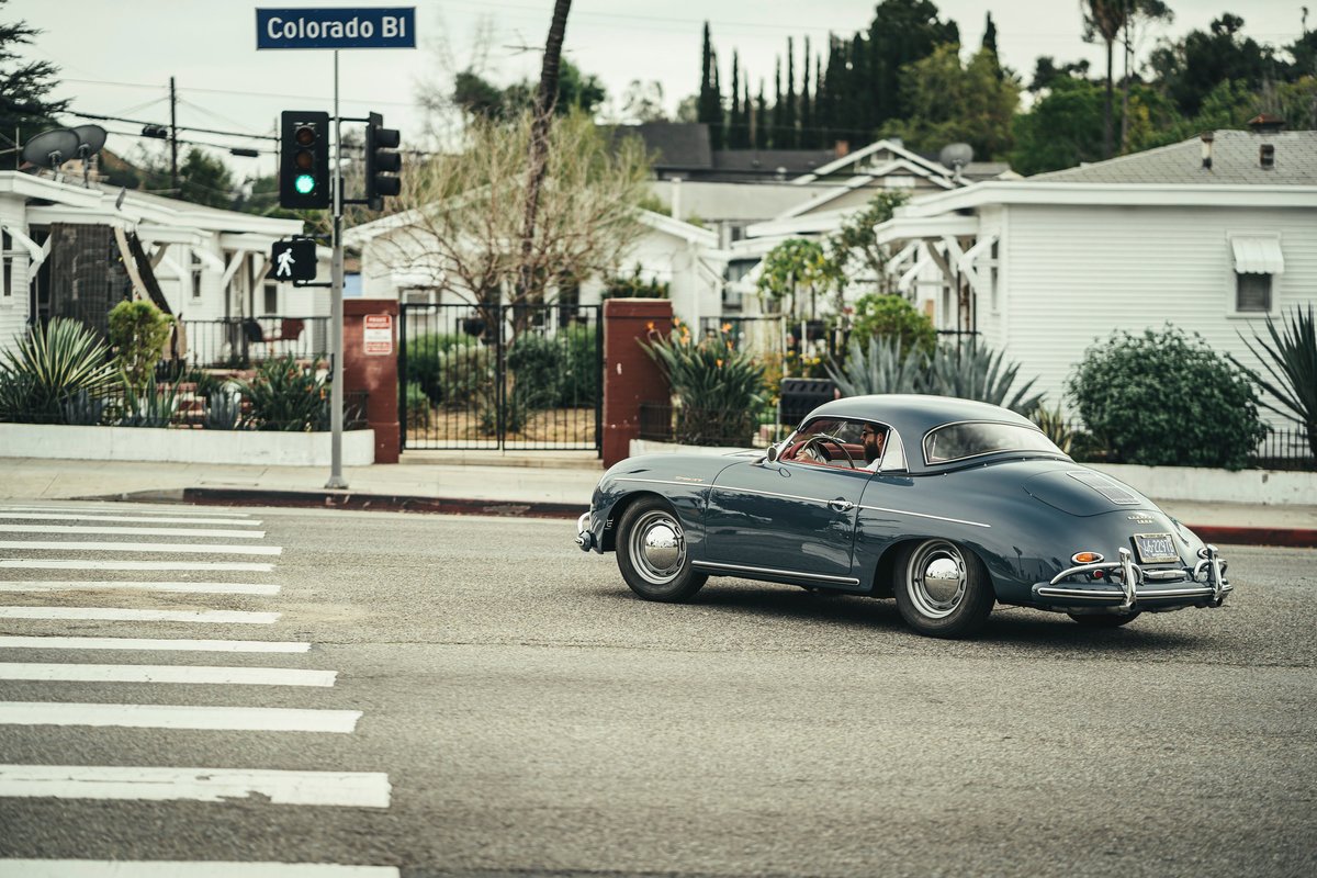 Vintage slate blue Porsche 356 Coupe, featuring chrome trim and full-disk hubcaps, drives on Colorado Blvd, Los Angeles.