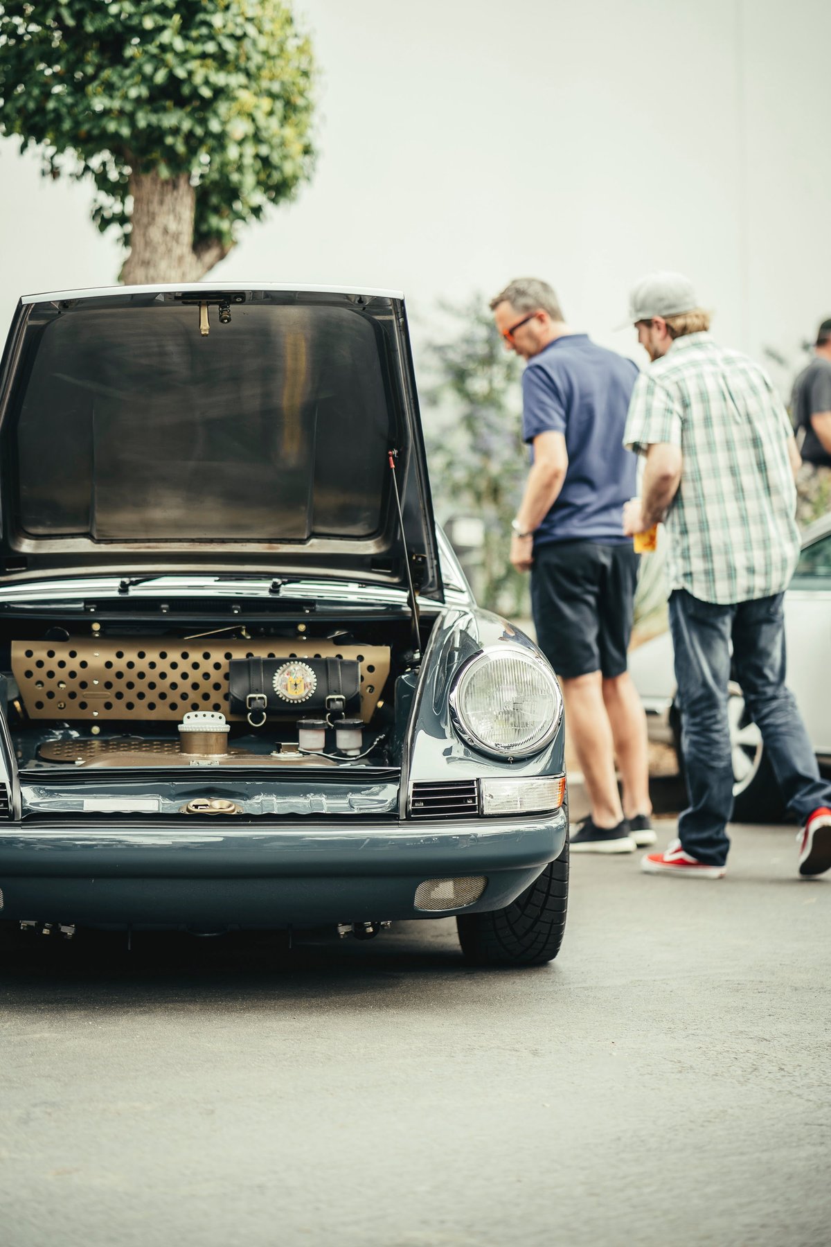 Slate Grey classic Porsche 911, frunk open revealing custom tan perforated panel, leather trim & accessories at a car show.