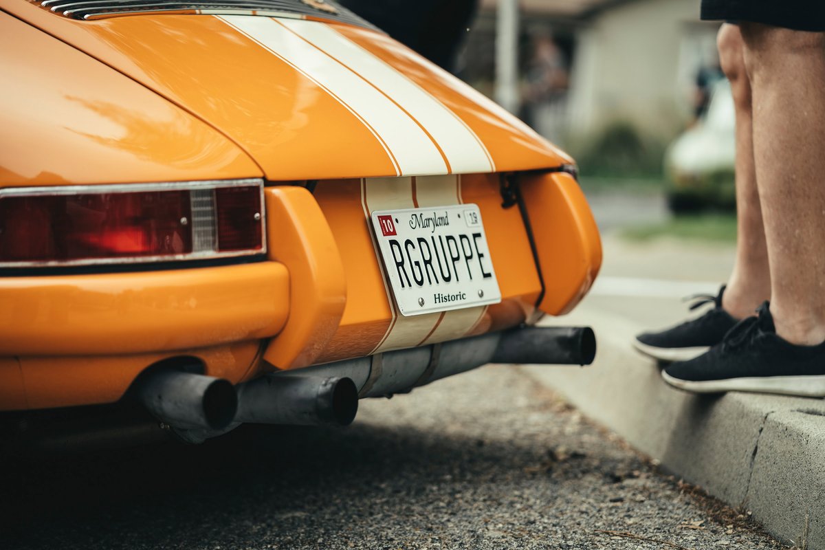 Rear view of an orange RGruppe Porsche 911 (long-hood) with white livery stripes, vintage taillight, and dual exhausts.