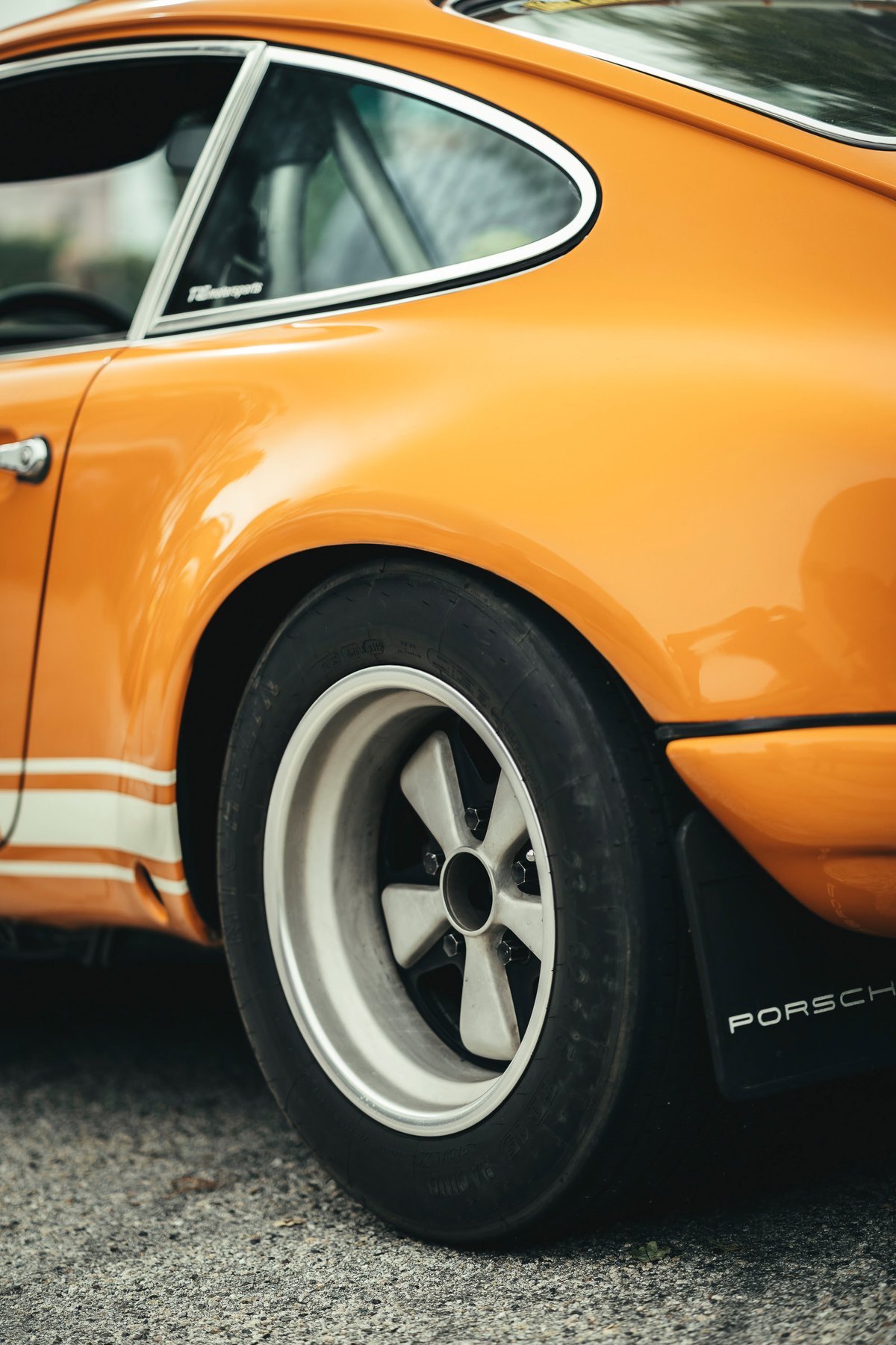 Tangerine Porsche 911 rear quarter. Classic Fuchs rims, track tires, white side livery, chrome window trim, roll cage.