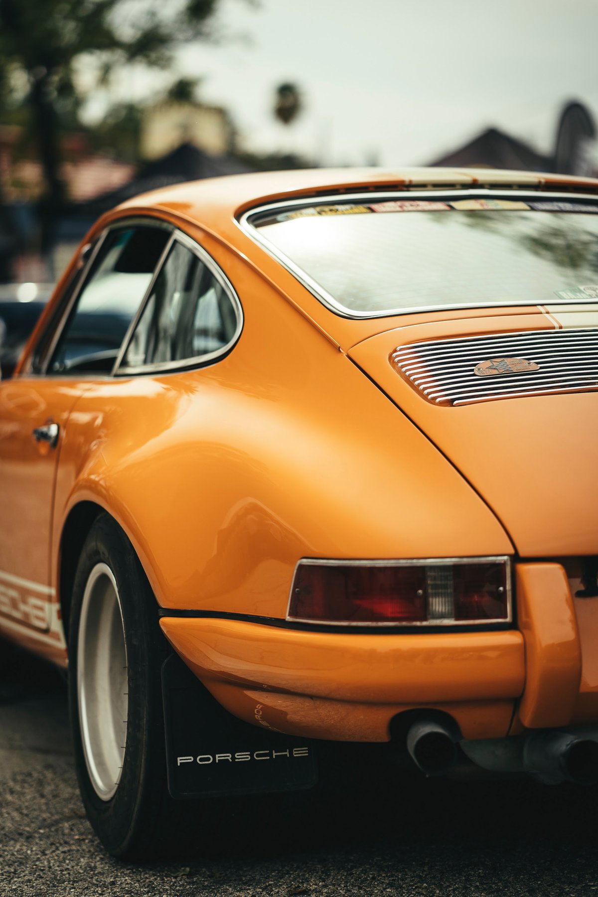 Signal Orange vintage Porsche 911 with white side livery, Fuchs-style rims, chrome trim, and Porsche mudflaps.