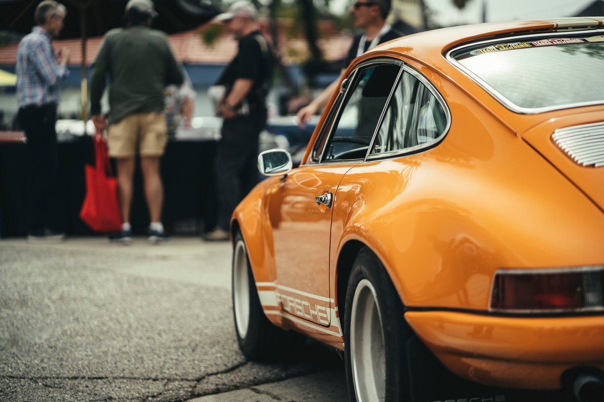 Tangerine Porsche 911 with white "PORSCHE" side livery, chrome trim, and white Fuchs-style rims. Lit Show LA.