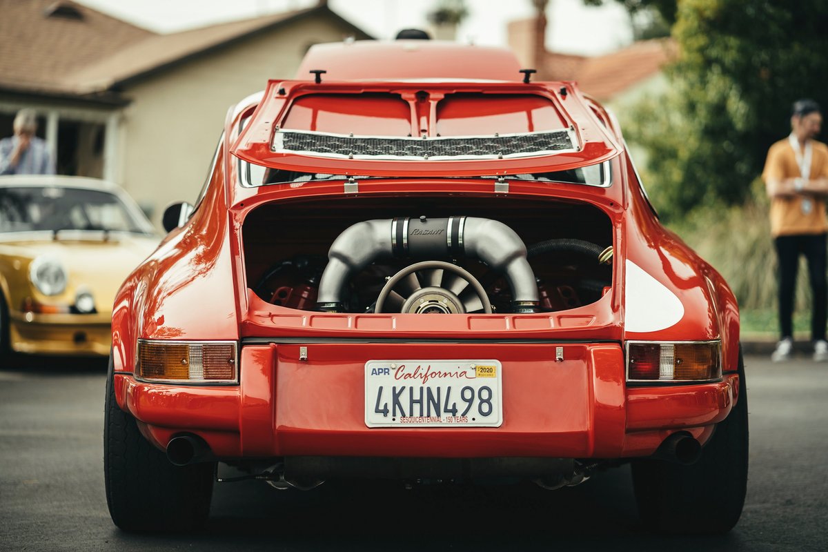 Rear view of a red air-cooled Porsche 911, engine lid open revealing its flat-six. Features widebody fenders and white racing livery.