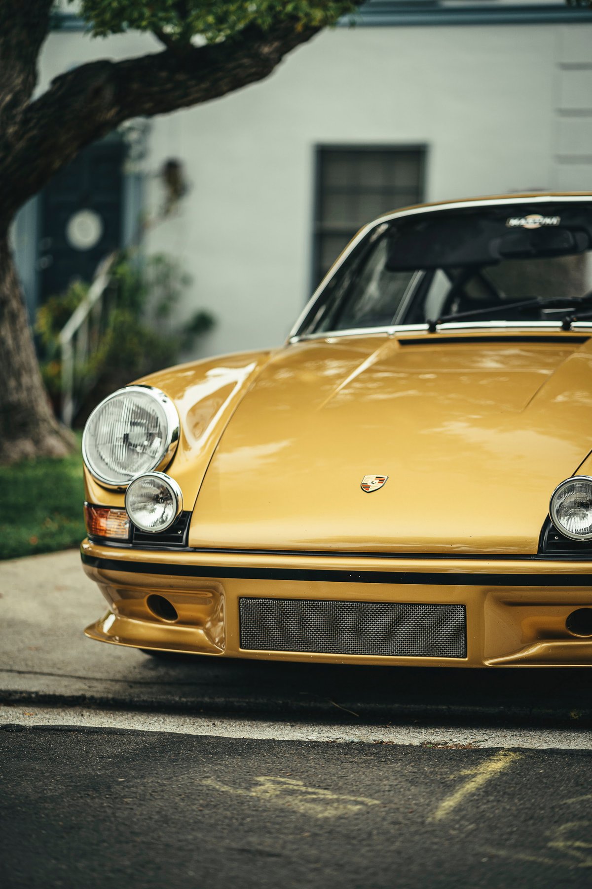 Radiant gold classic Porsche 911 showcasing its iconic round headlights, front spoiler, mesh grille, and Porsche crest.