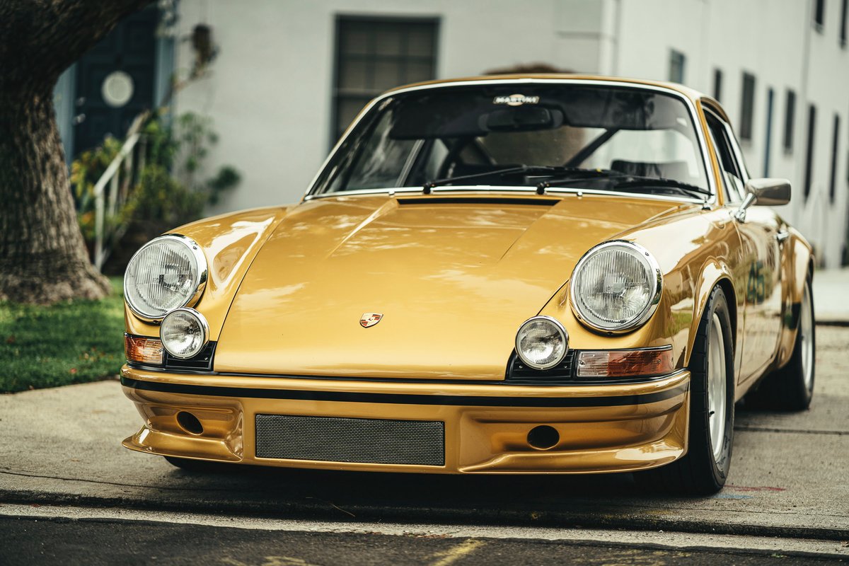 Gold wide-body classic Porsche 911 with custom front spoiler, auxiliary lights, Martini banner, and Fuchs-style performance rims.