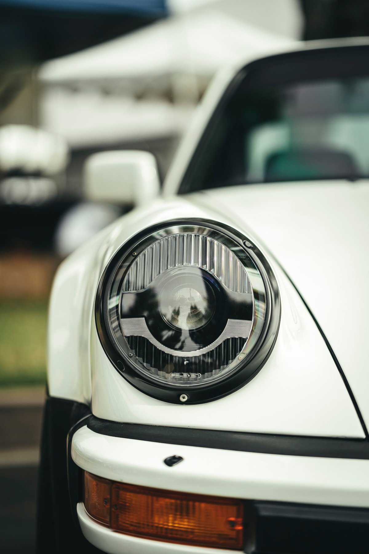 White classic Porsche 911's modern LED headlight with fluted lens, amber turn signal, and black bumper trim.