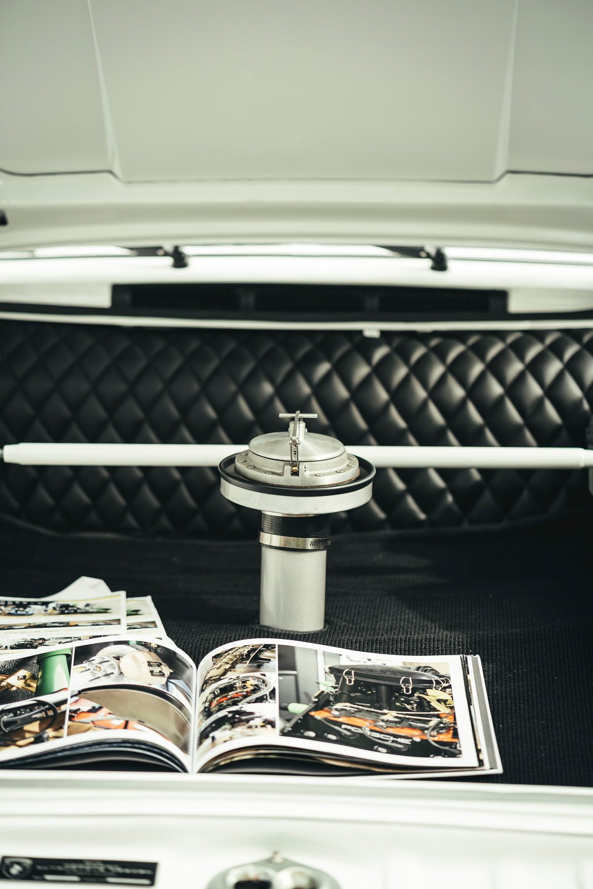 White air-cooled Porsche interior: vintage aluminum race fuel filler, quilted black leather bulkhead, and white strut bar.
