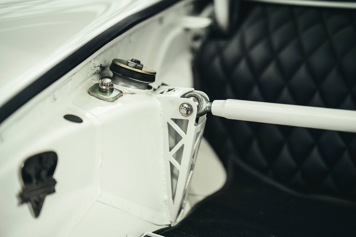 White Porsche 911 (air-cooled) strut tower with custom lightweight strut bar, spherical bearing mount. Black quilted interior.