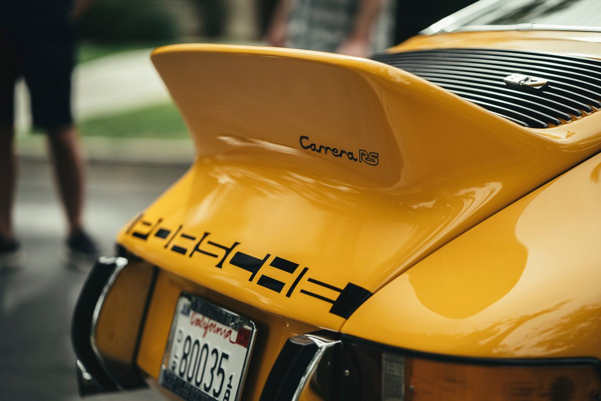 Close-up rear of a yellow Porsche 911 Carrera RS with whale tail spoiler and iconic PORSCHE decklid script livery.