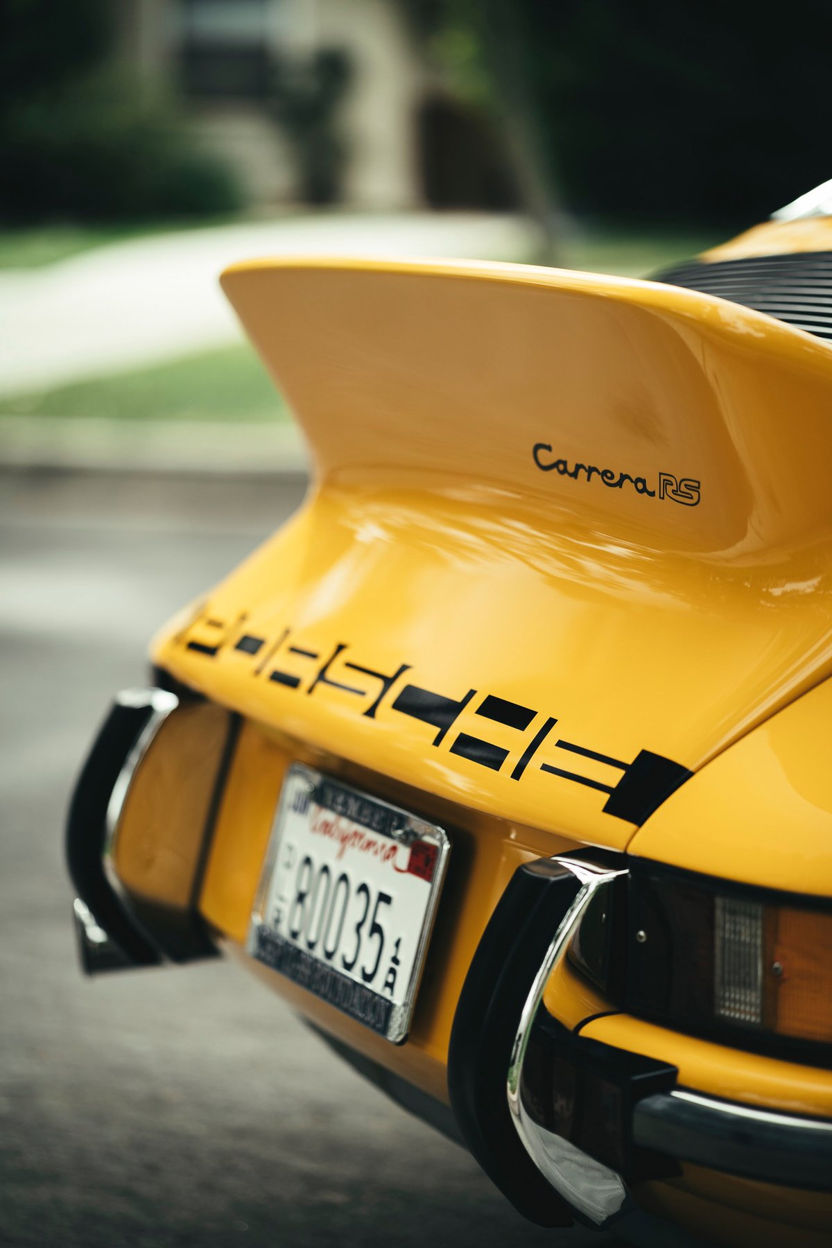 Vibrant yellow 1973 Porsche 911 Carrera RS rear with iconic ducktail spoiler, "PORSCHE" livery, and chrome bumperettes.