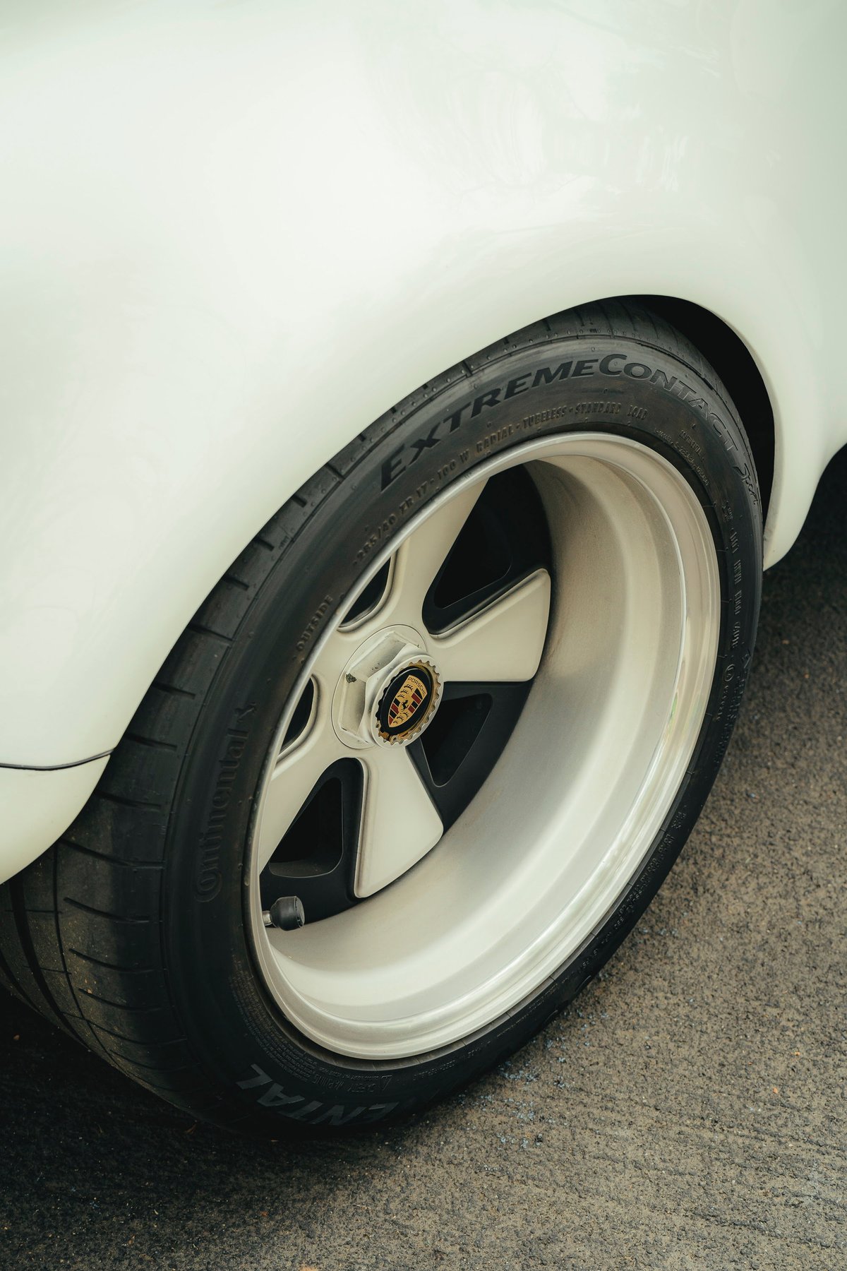 White classic Porsche rear wheel: Fuchs-style multi-piece rims with polished lip, Porsche crest centerlock, & Continental ExtremeContact tires.