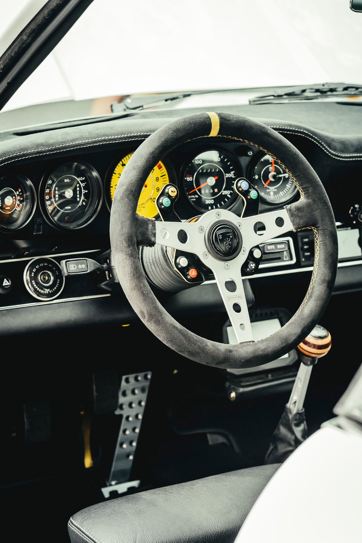 Singer 911 interior: Alcantara steering wheel with yellow stripe, bespoke yellow gauges, wood shift knob, and drilled pedals.