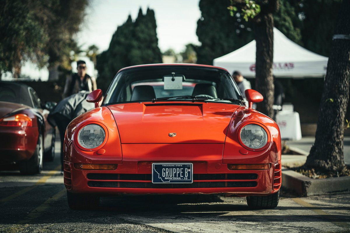 Front view of a Guards Red Porsche 959 supercar at the Los Angeles "Lit Show." Features "GRUPPE B" plate & iconic round headlamps.