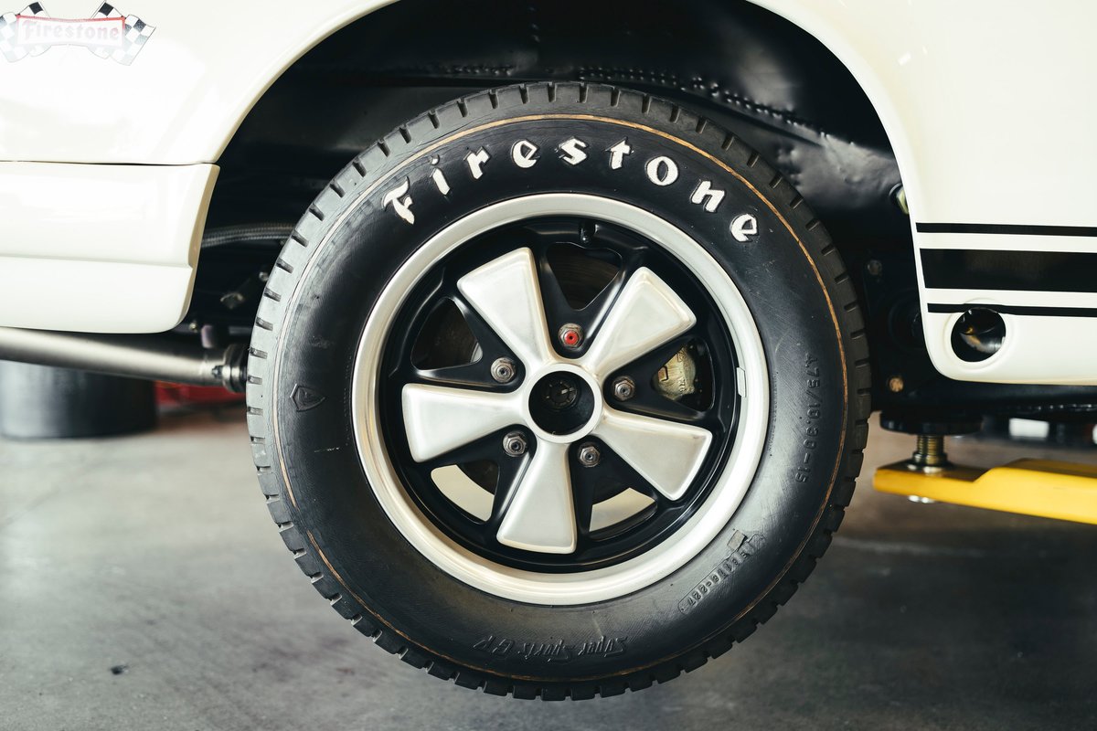 White Porsche 911 with classic two-tone Fuchs rims, Firestone white-letter tires, and black racing stripes livery.
