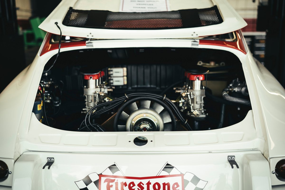 White vintage Porsche 911 race car. Exposed air-cooled flat-six engine with dual carbs, cooling fan. Firestone racing livery.