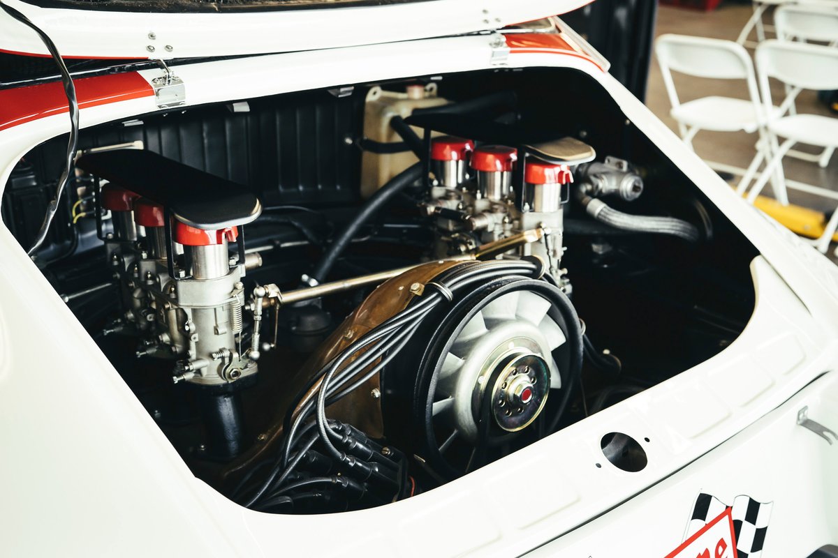 Classic white Porsche 911's air-cooled flat-six engine with dual carburetors, red racing stripe livery visible in engine bay.