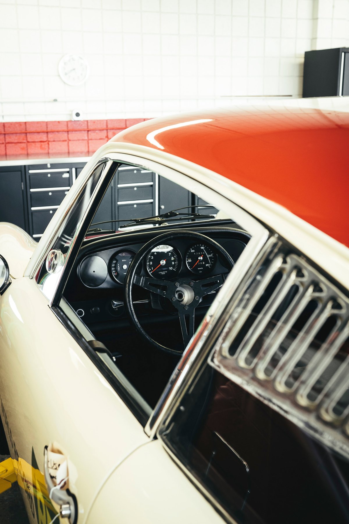 Classic Porsche 911 with two-tone red & cream livery. View of the vintage interior with 3-spoke steering wheel and louvered quarter window.