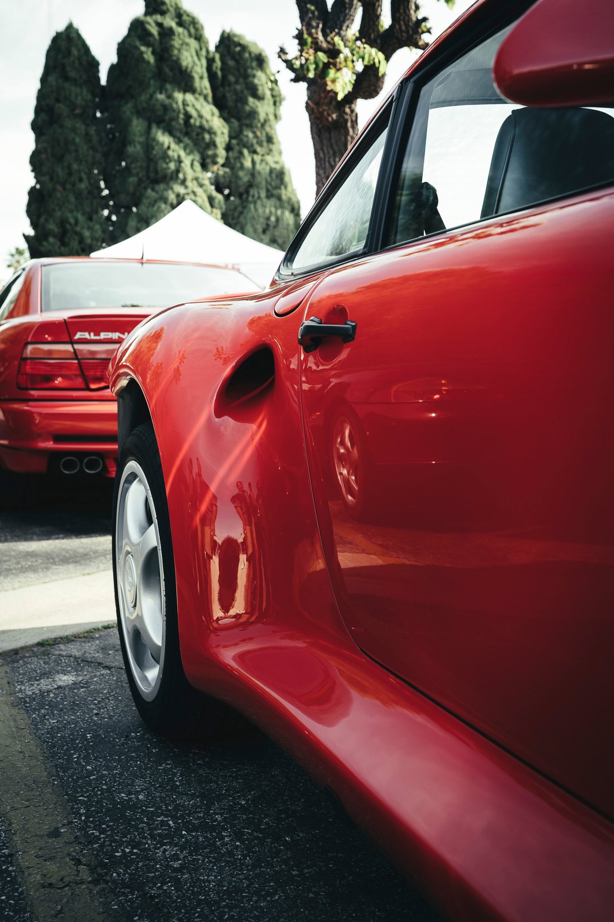 Vibrant red Porsche 959 at a Los Angeles show, showcasing its wide body, iconic side intake, black trim, and OEM silver rims.