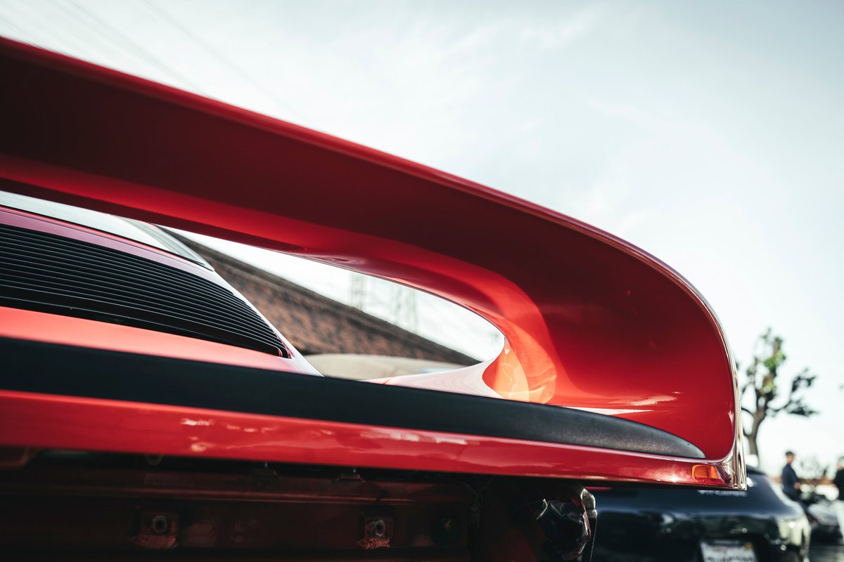 Close-up of a vibrant red Porsche 964 Turbo, showcasing its large, iconic whale tail spoiler and black engine grille.