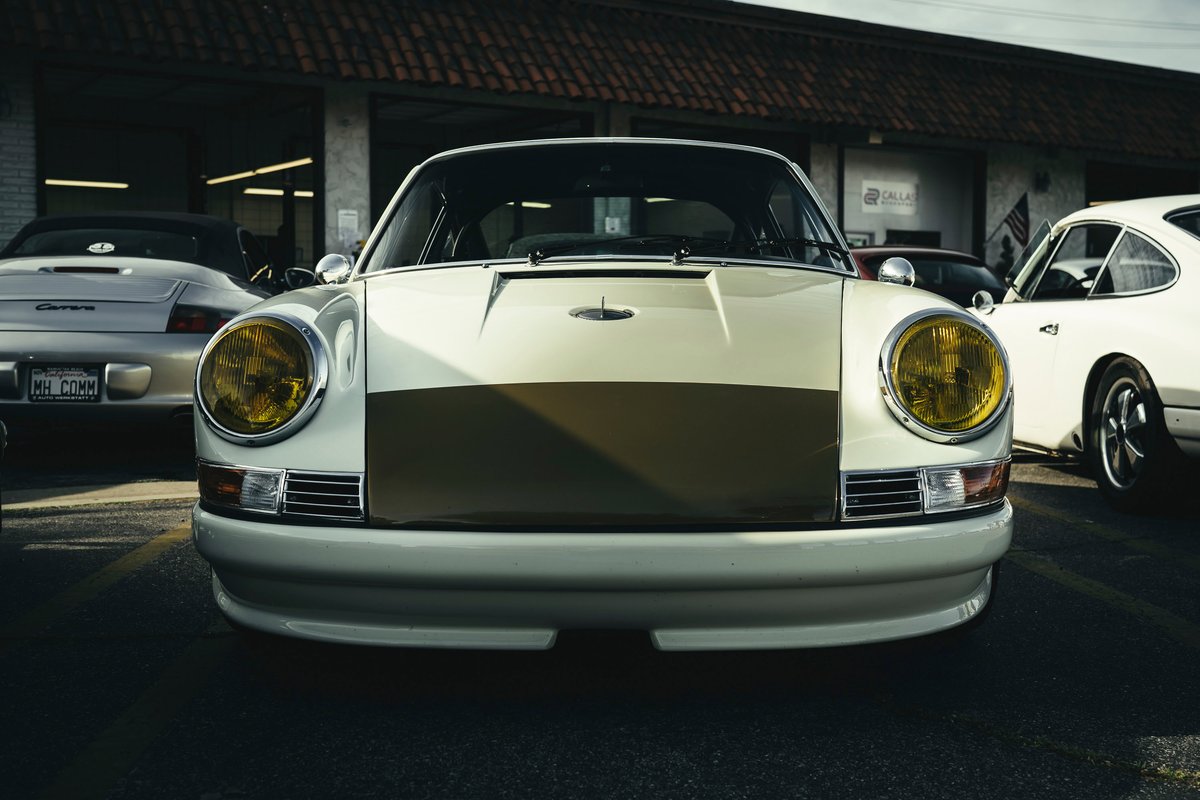 Front view of custom cream air-cooled Porsche 911 with olive stripe livery, yellow headlights, and integrated front valance.