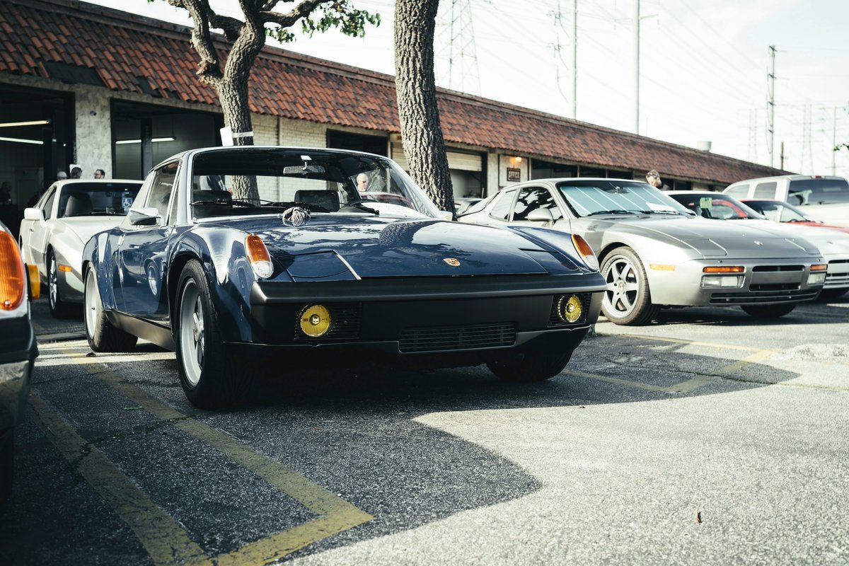 Midnight blue Porsche 914 Targa with yellow fog lights, black trim, and silver Fuchs rims at a Los Angeles show.