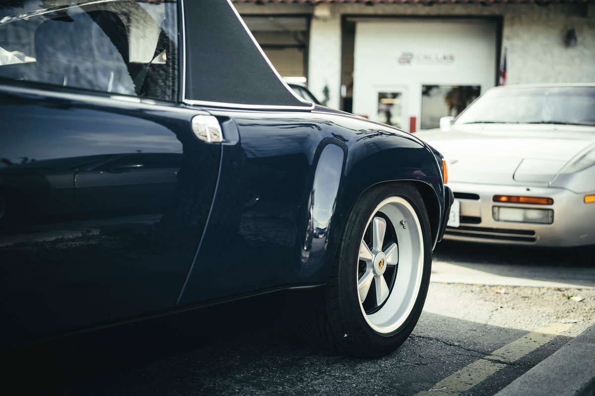 Dark blue Porsche 914 with white-centered Fuchs wheels and targa top, a Porsche 944 behind.