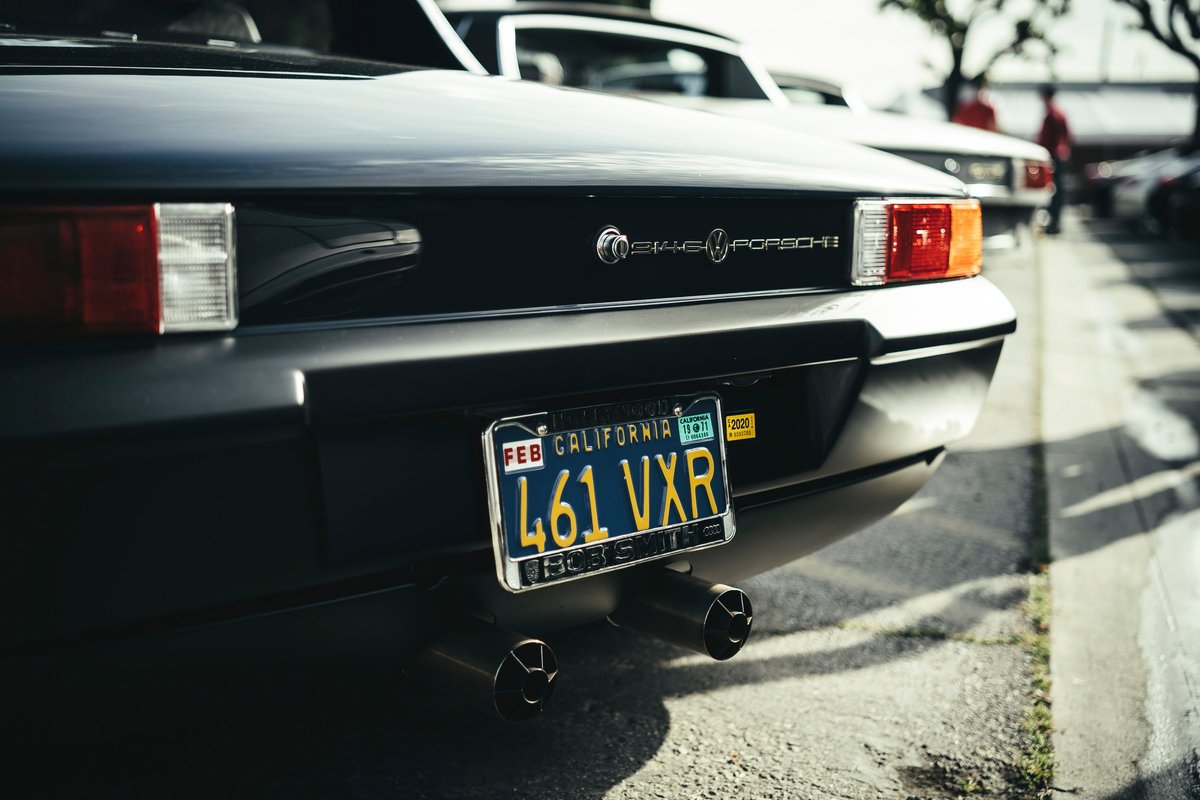 Close-up of a black VW-Porsche 914 rear, 'VW-Porsche' badging, rectangular taillights, CA plate & dual black exhaust tips.