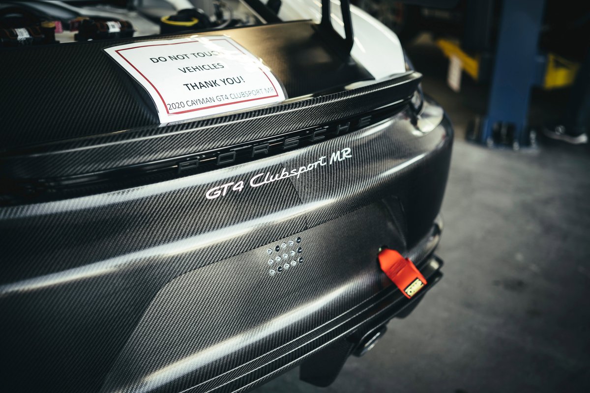 Close-up of a 2020 Porsche Cayman GT4 Clubsport MR's exposed carbon fiber rear fascia and decklid with a bright orange tow strap.