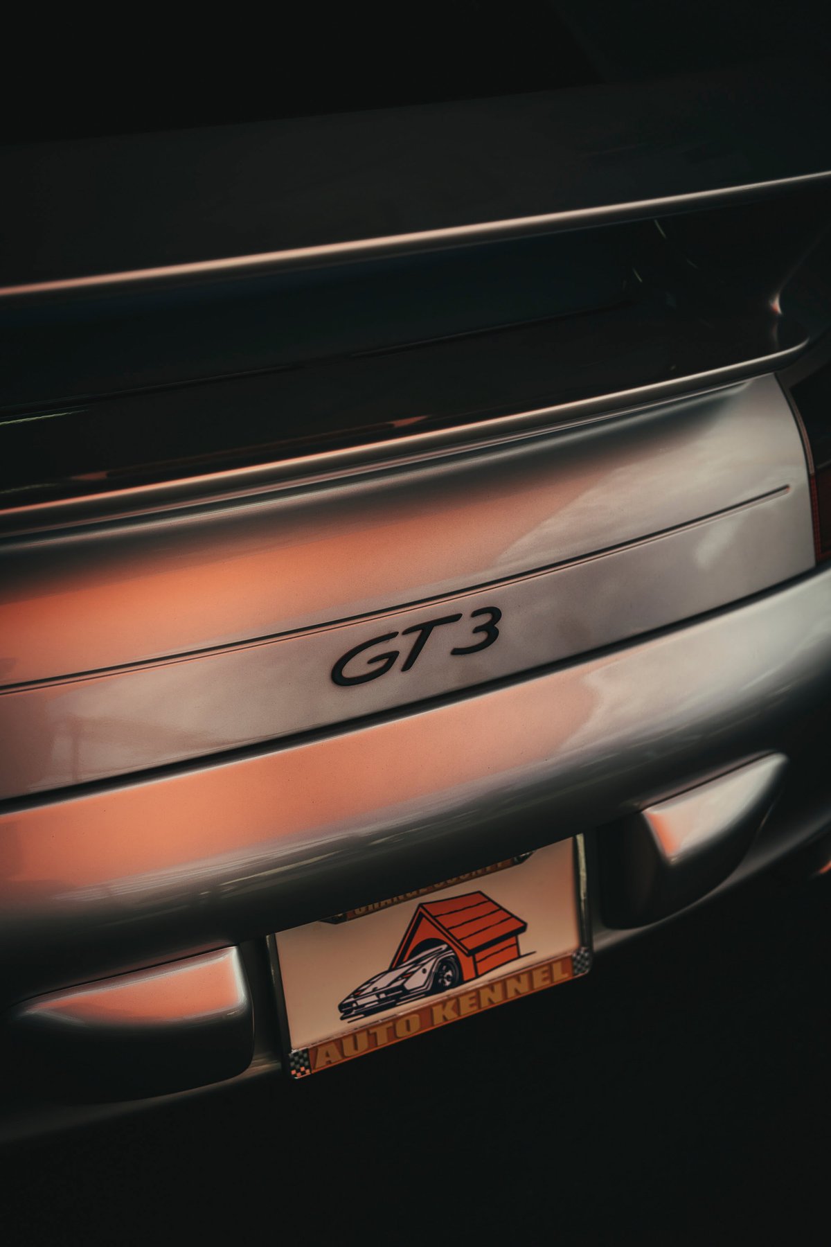 Silver Porsche 911 GT3 rear, featuring its distinctive GT3 badge, sleek rear spoiler, and "Auto Kennel" plate frame.