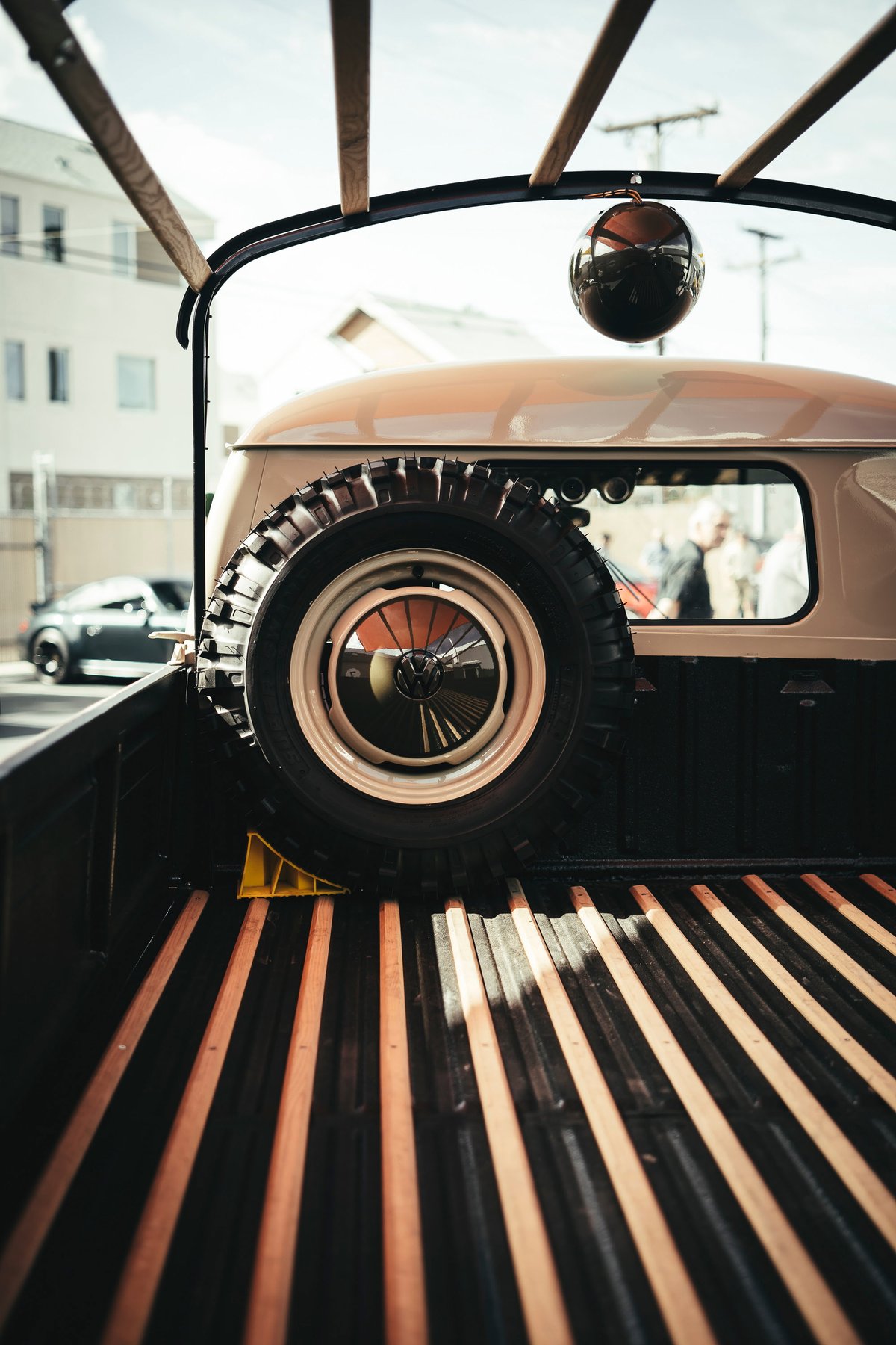 Vintage beige VW Type 2 Single Cab pickup bed, featuring a spare tire with VW hubcap, steel rim, and wood slats. Lit Show LA.