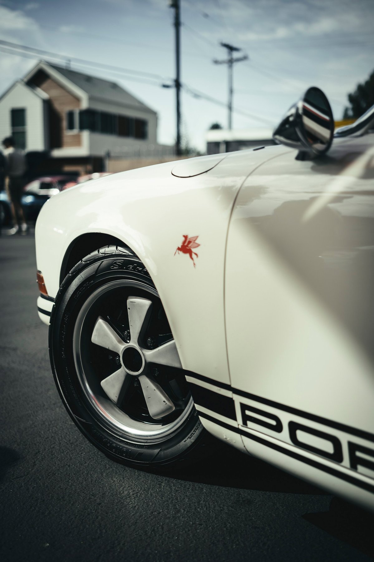 White classic Porsche 911 with iconic Fuchs wheels, red Mobil Pegasus fender badge, and black PORSCHE side livery.