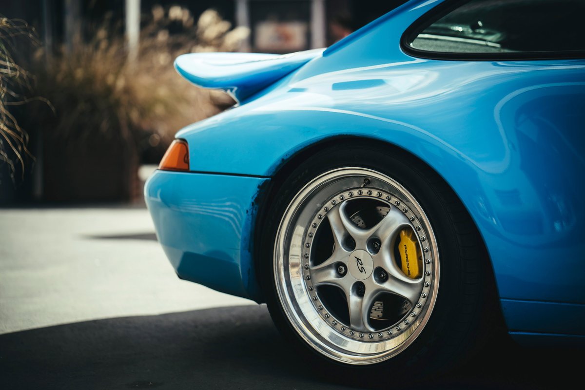Riviera Blue Porsche 993 rear quarter, featuring a ducktail spoiler, multi-spoke RS-style rims, and yellow brake calipers.
