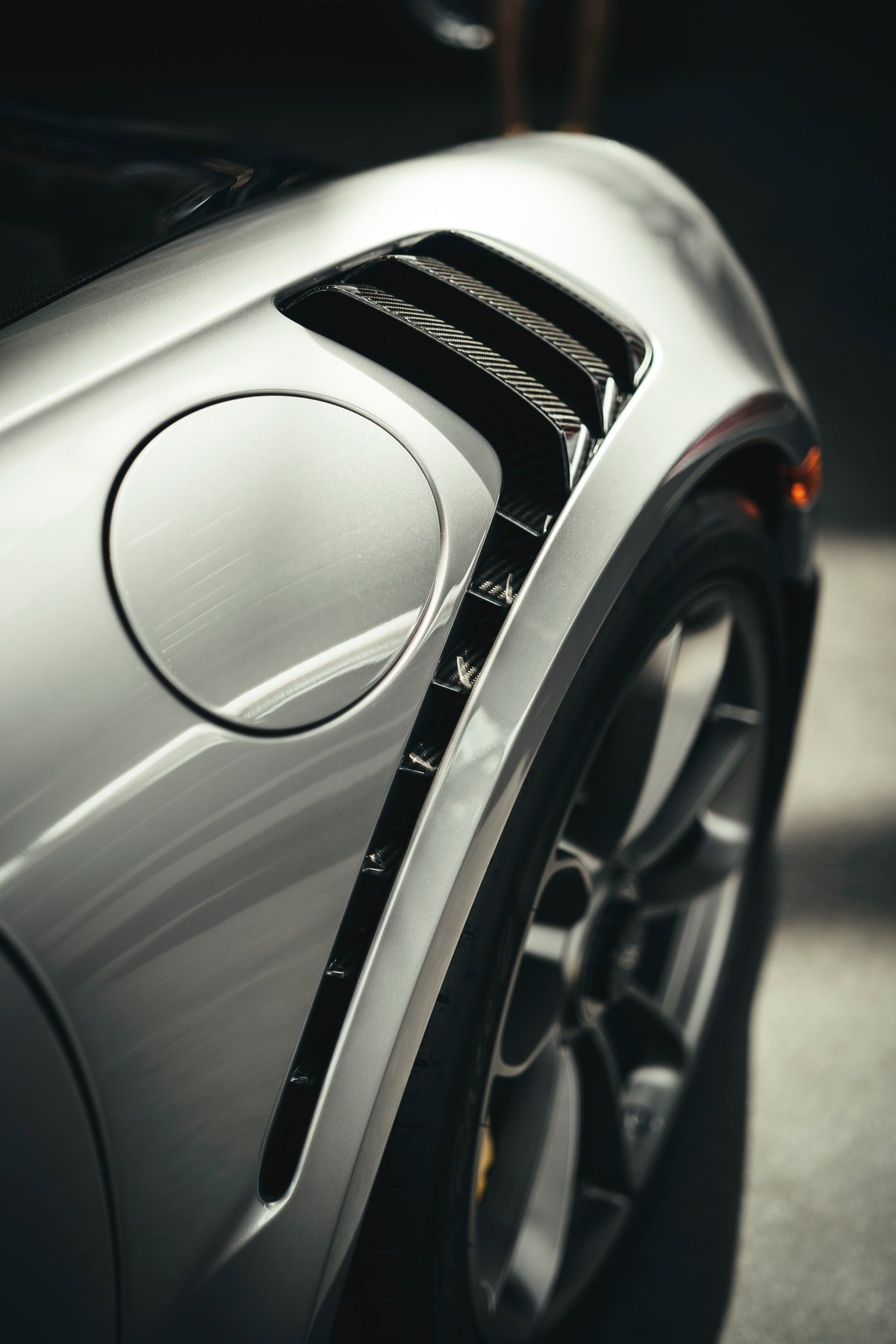 Close-up of a silver Porsche 911 GT3 RS (991.2) rear quarter panel, featuring carbon fiber fender vents, fuel filler, and alloy wheel.