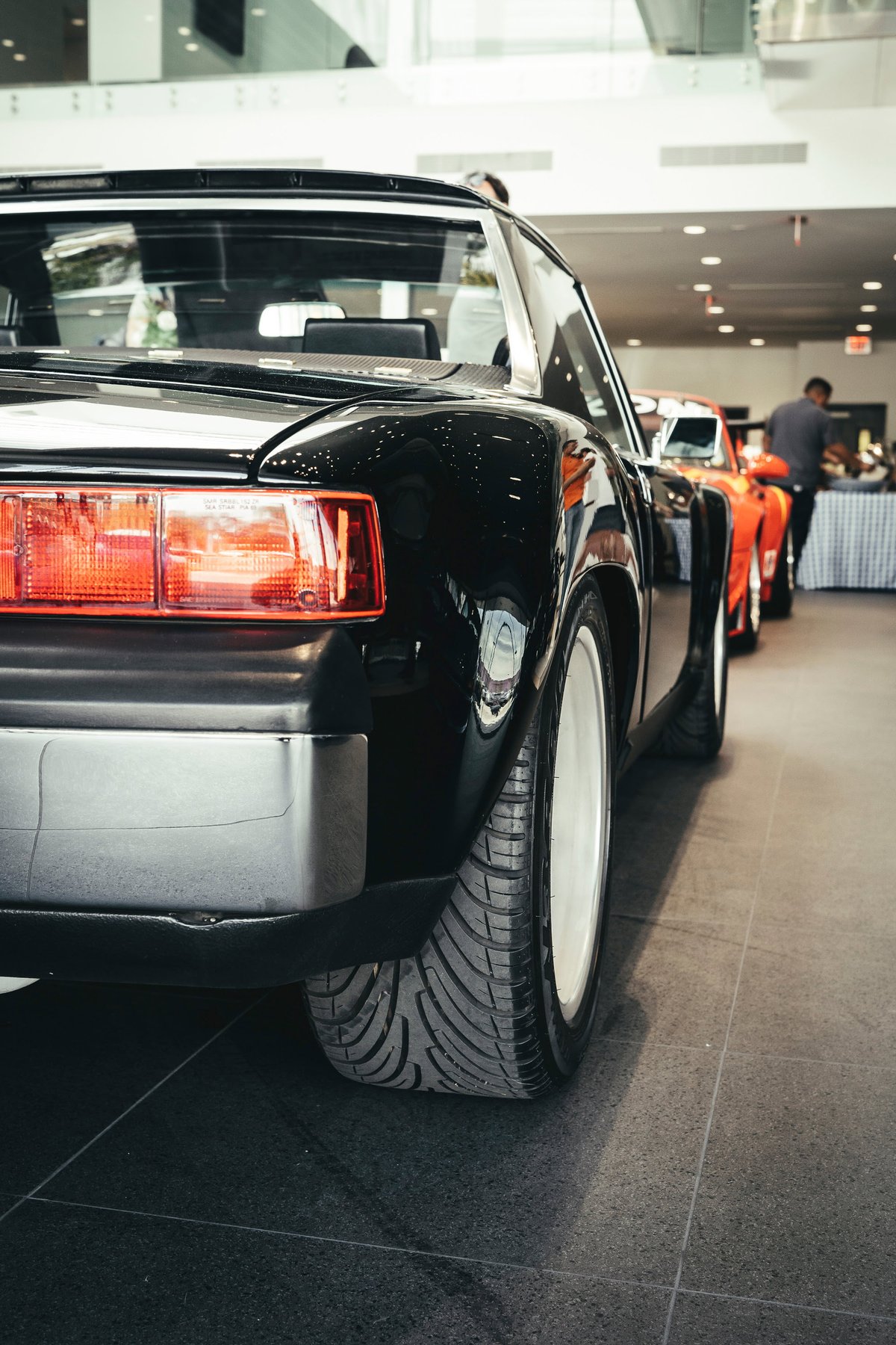 Gloss black Porsche 911 Targa, G-series rear. Wide white rims, aggressive tire tread, and classic red taillights at show.