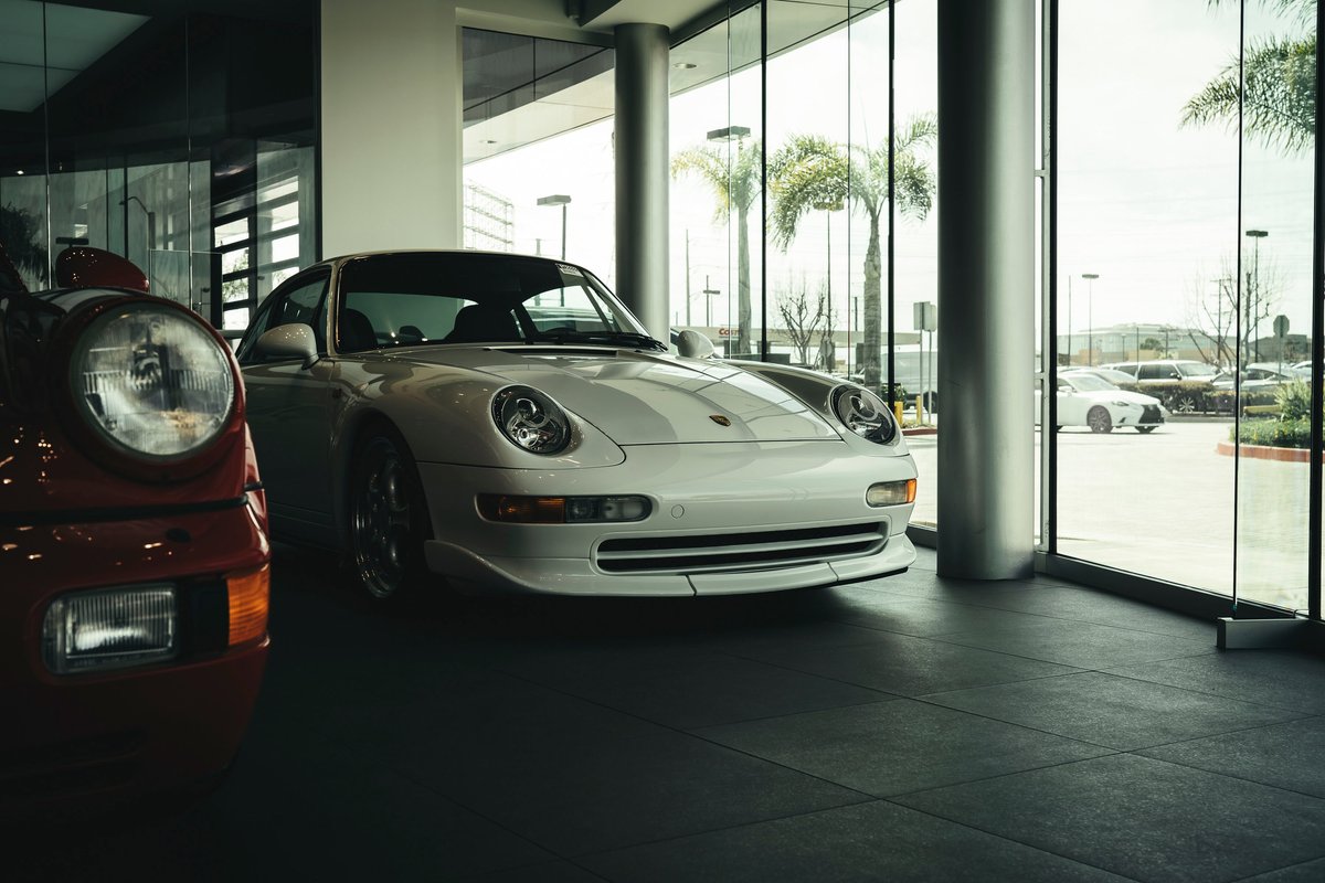Classic white Porsche 911 (993) on display, featuring its iconic body-integrated headlights, aero front lip, and multi-spoke rims.