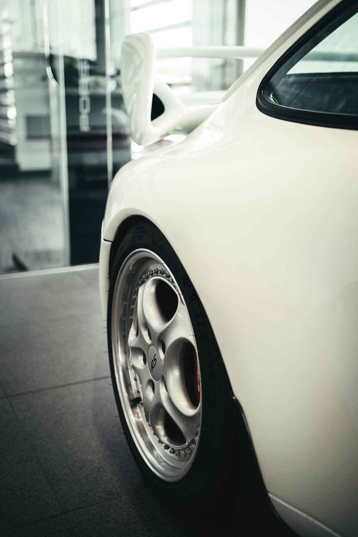 Rear quarter of a white Porsche 993 Carrera RS, showcasing its iconic whale tail wing and multi-piece BBS RS wheels with red calipers.