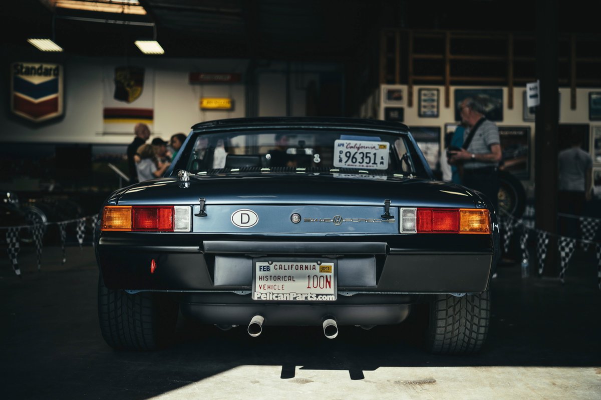 Classic dark blue Porsche 914 targa rear, showing square taillights, black bumper, dual exhaust, and CA historical plates.