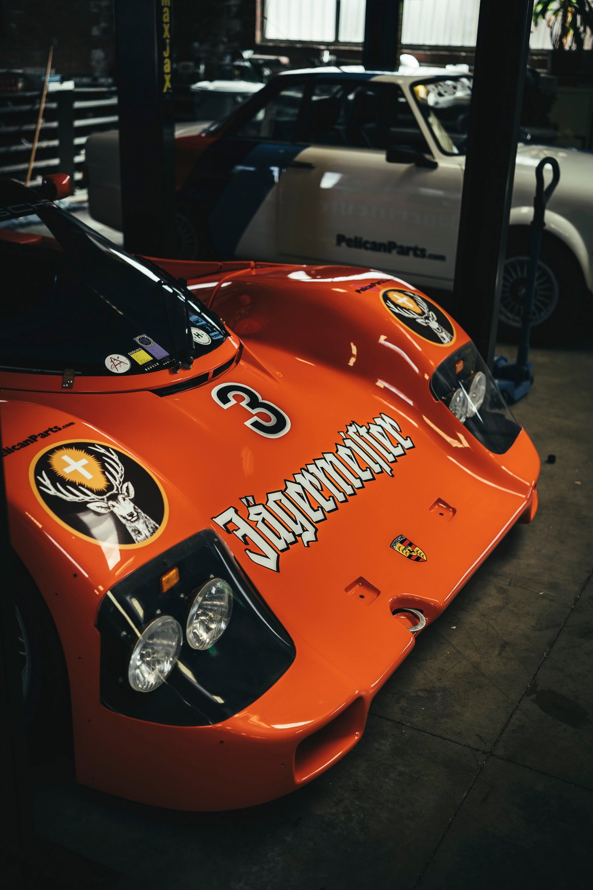 Orange Porsche 962 Group C race car with Jägermeister livery & #3, showcasing its aerodynamic front bodywork & integrated headlights.