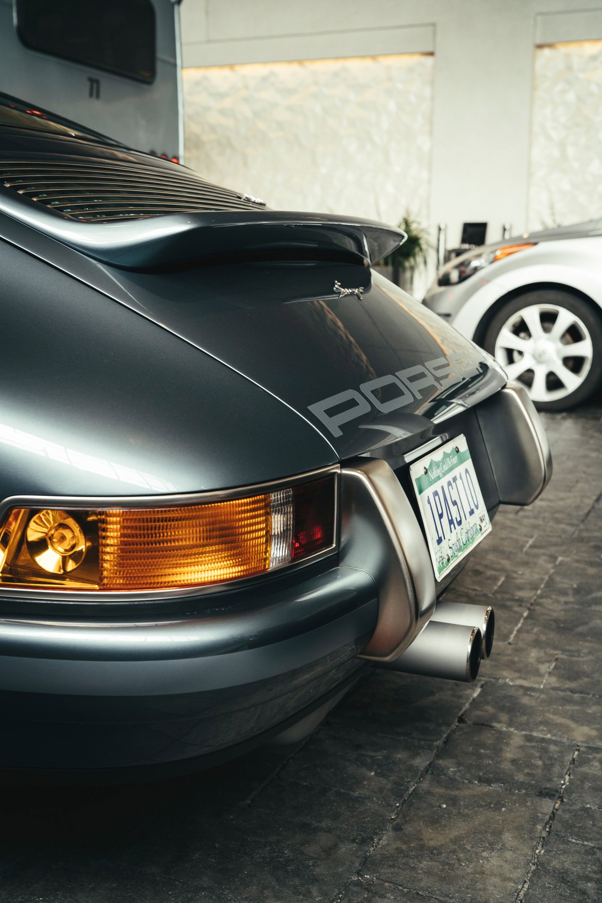 Dark gray classic Porsche 911 G-body rear. Features whale tail spoiler, impact bumpers, "PORSCHE" script, and dual exhaust tips.