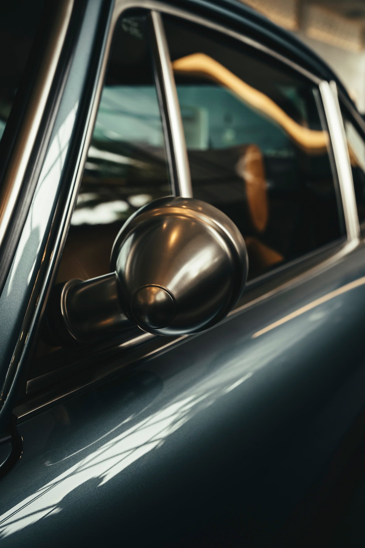 Air-cooled Porsche 911's dark metallic grey body, polished chrome bullet mirror, and brightwork window trim.