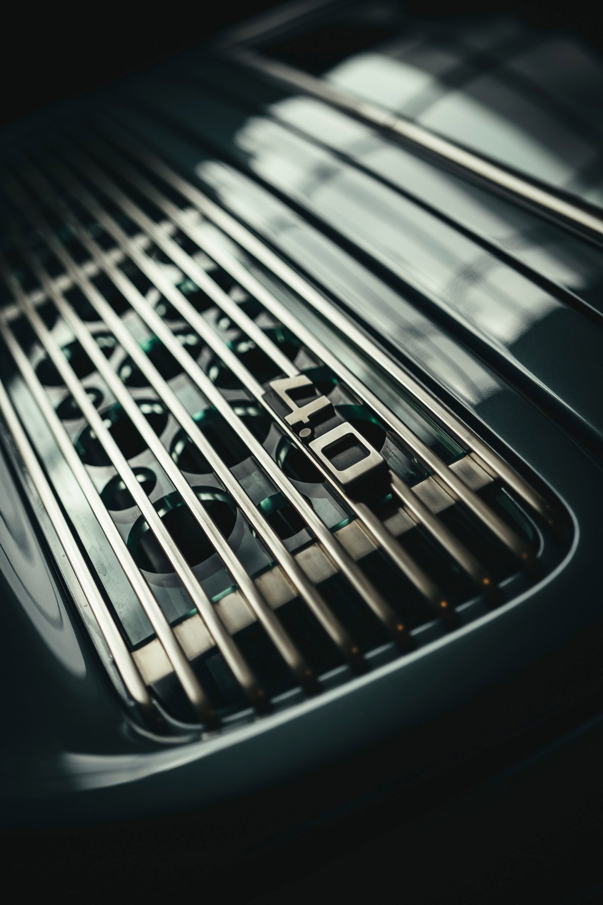 Close-up of a deep-hued Porsche 911 GT3 RS 4.0 rear decklid. Polished horizontal cooling slats reveal the engine bay, highlighting the 4.0 badge.