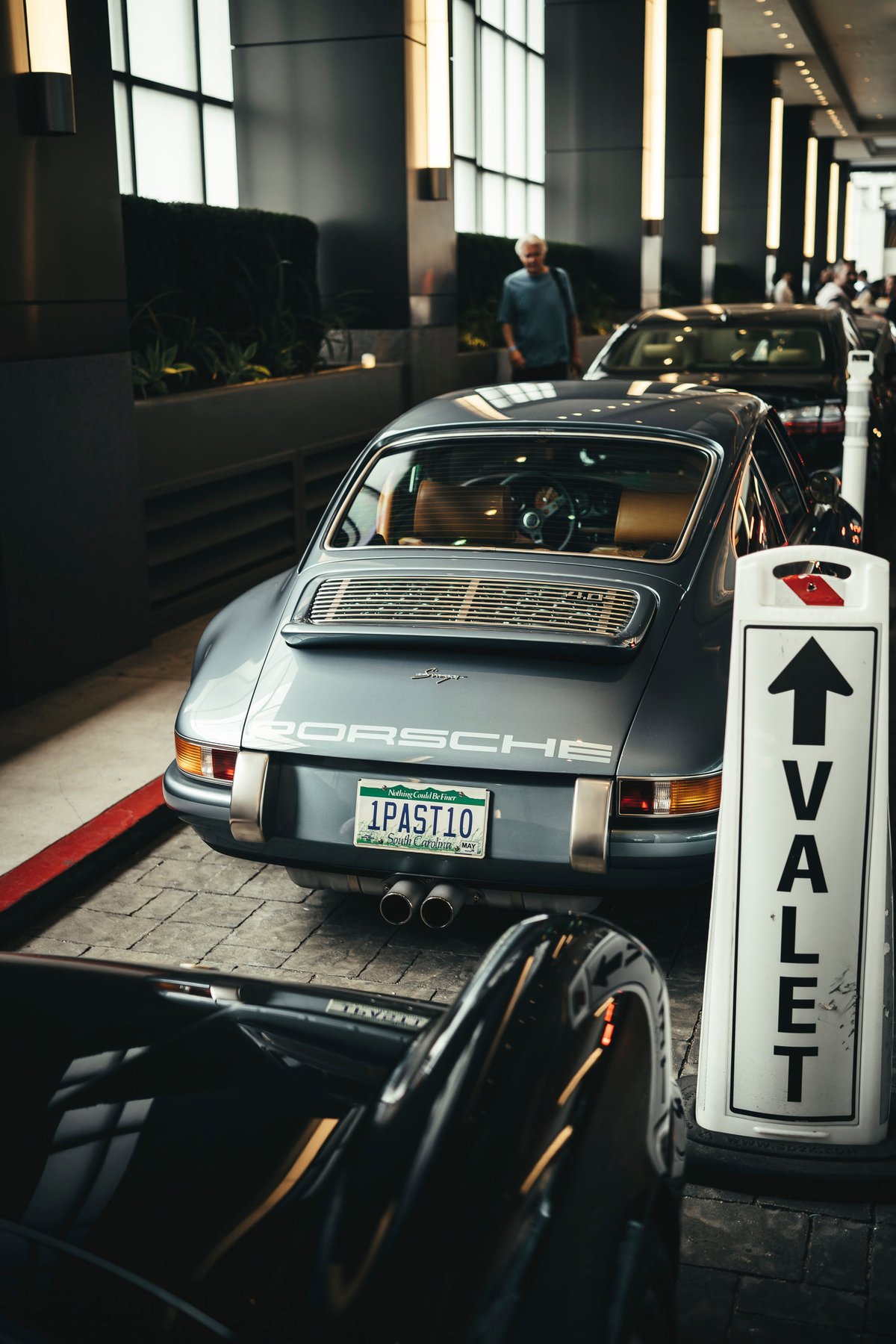 Classic Slate Grey Porsche 911S with tan interior, chrome trim, and dual exhaust at a Los Angeles valet.